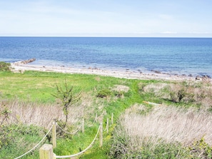 A coastal landscape with a sandy beach, grassy areas, and a wooden fence.