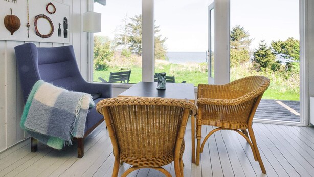 A room with a blue armchair, wicker chairs, a table, and a view of the outdoors.