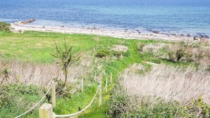 A coastal landscape with a sandy beach, grassy areas, and a wooden fence.