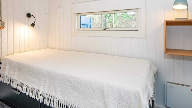 A bedroom with a single bed, a window, a wall-mounted lamp, and a radiator.