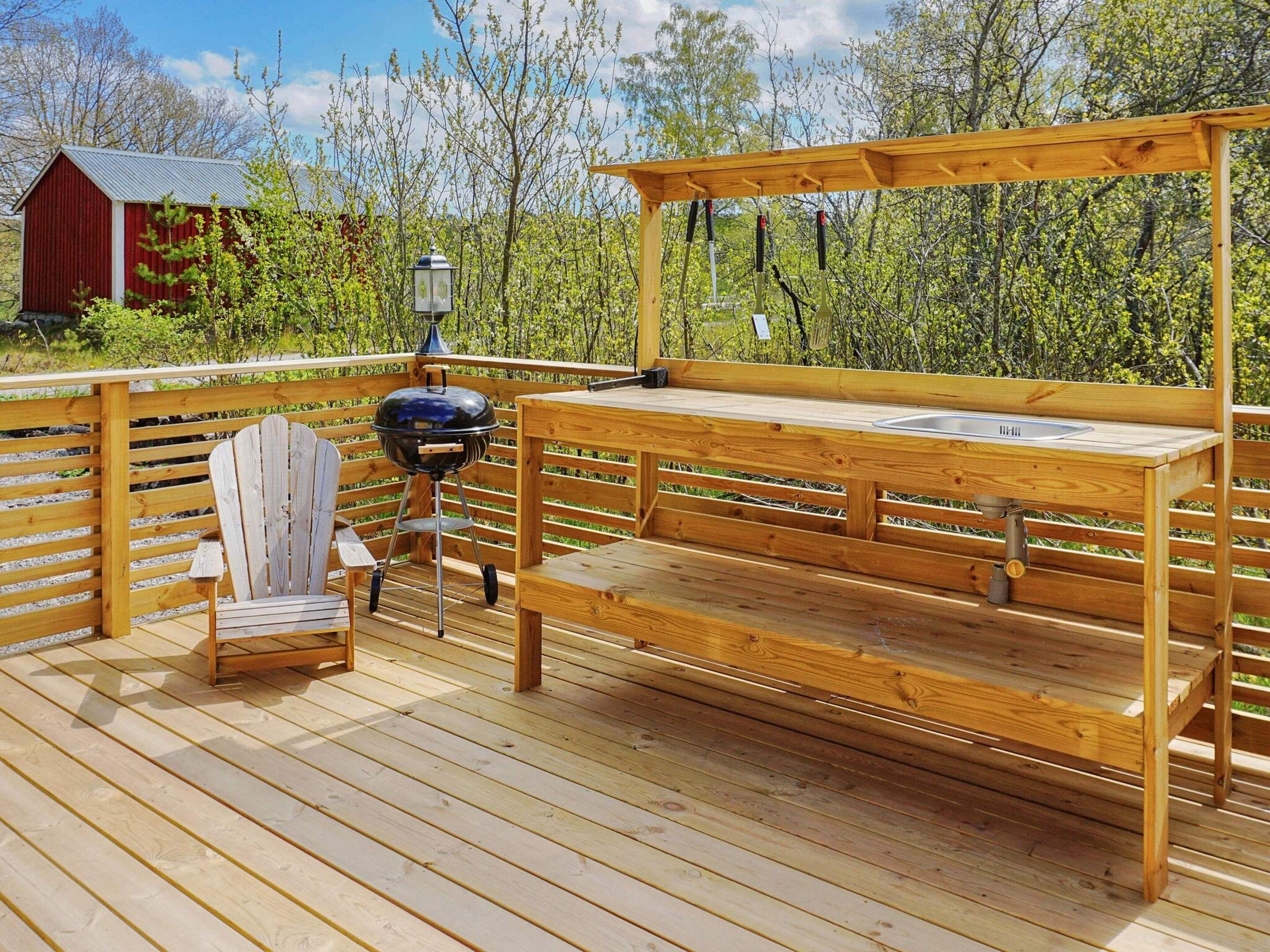 Une terrasse en bois avec un banc, un barbecue et une lanterne.
