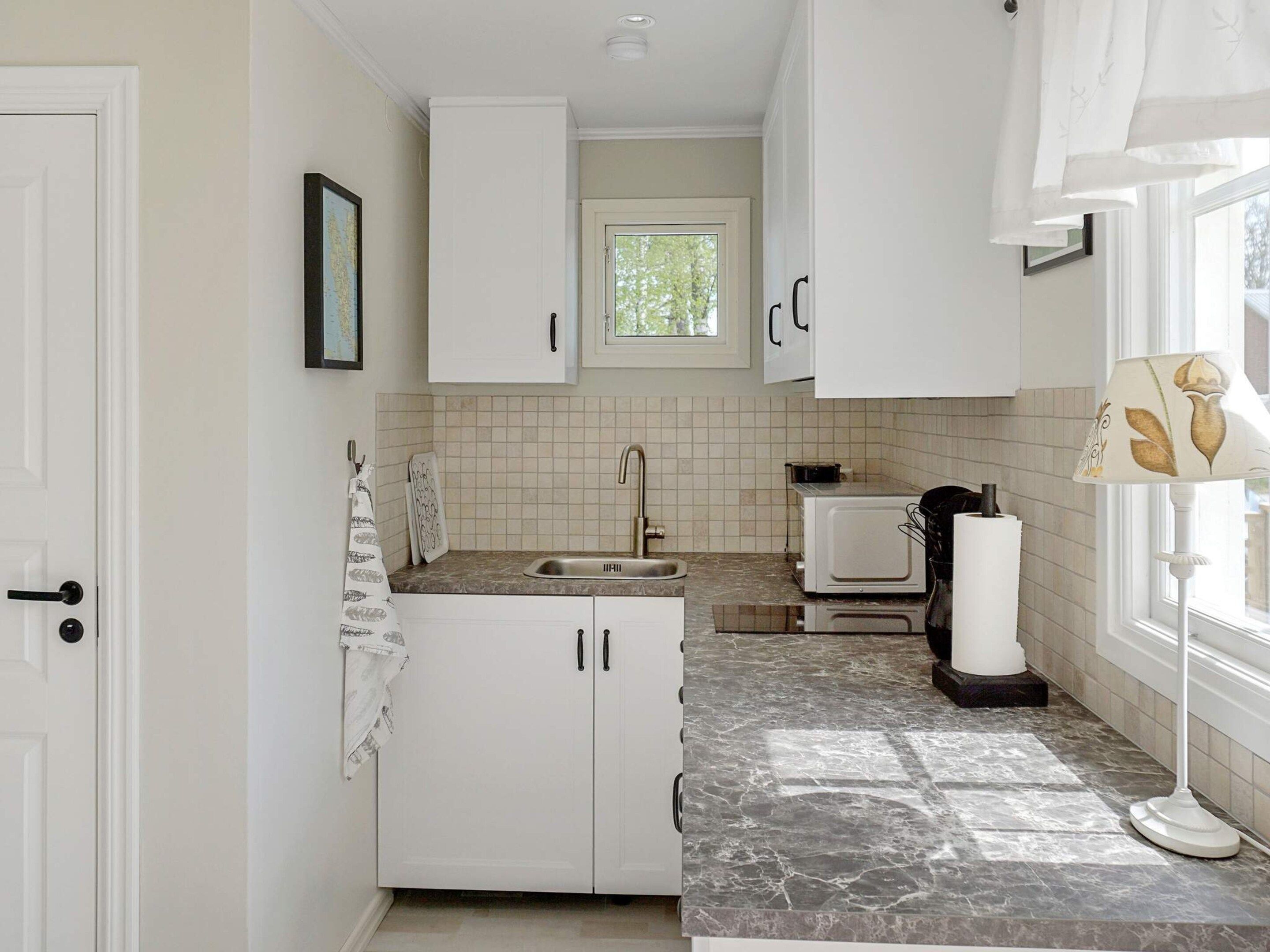 Una cocina con armarios blancos, un lavabo, un microondas y una ventana con cortinas.
