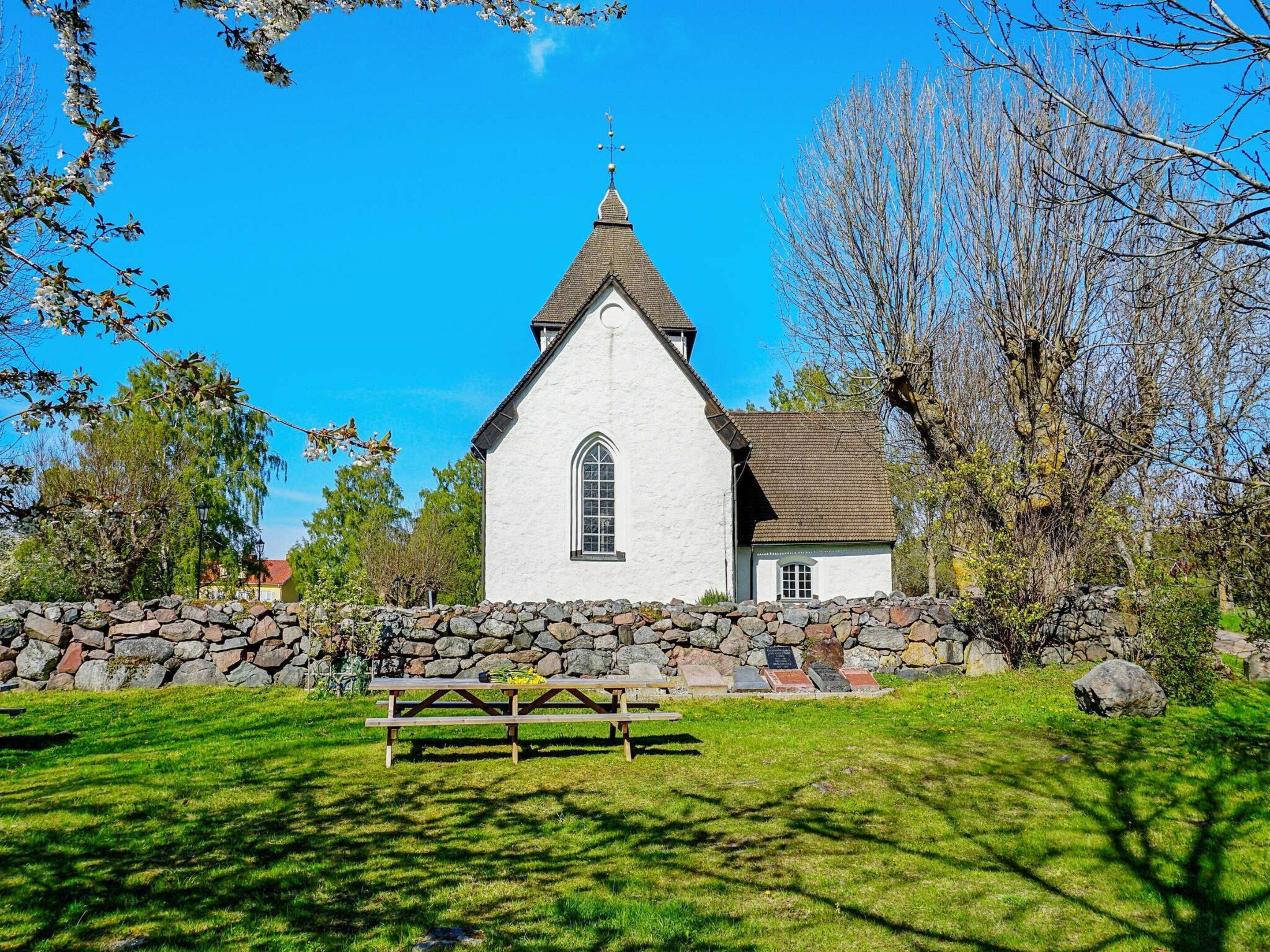 Eine weiße Kirche mit einem Spitzspitzboden, einer Steinmauer und einem Picknicktisch davor.