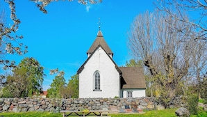 Une église blanche, dotée d’un clocher en forme de flèche, entourée d’un mur de pierre et agrémentée d’une table de pique-nique dans un espace verdoyant.