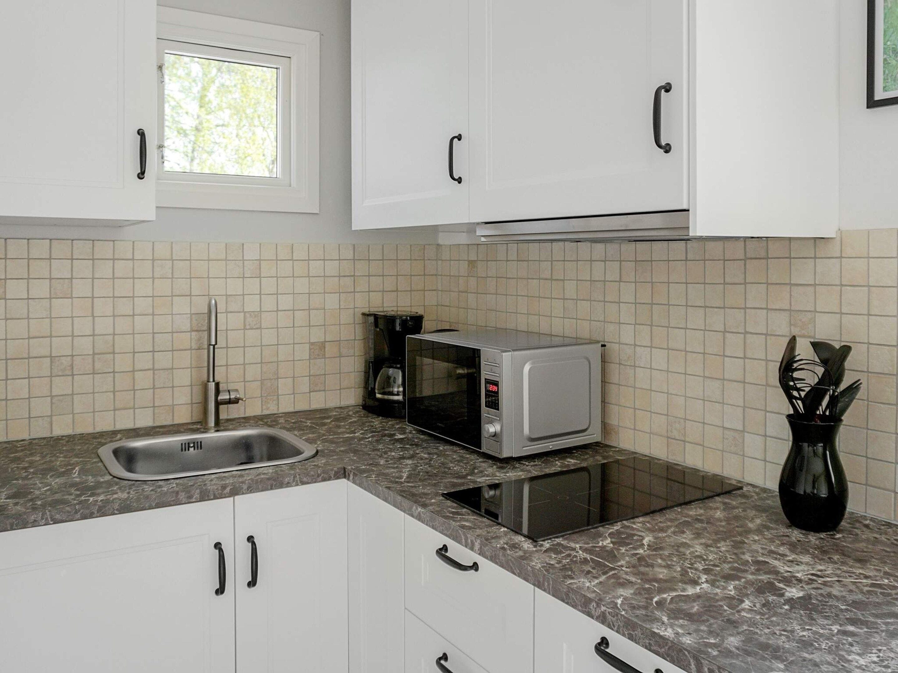 A kitchen with white cabinets, a sink, a microwave, and a coffee maker.