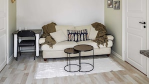 Un salon chaleureux avec un canapé, deux petites tables d’appoint, un fauteuil et un tapis blanc sur un plancher en bois.