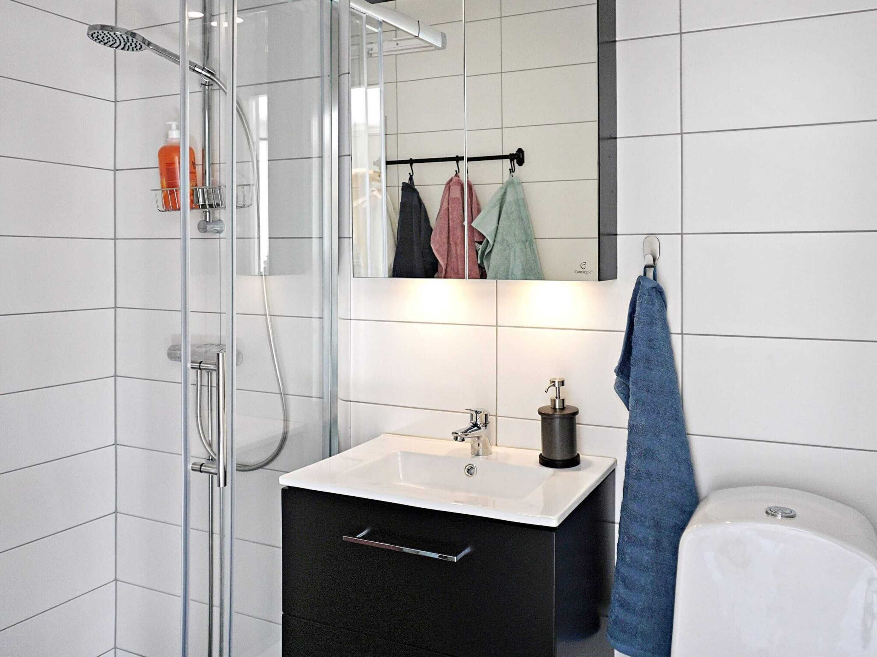 Een moderne badkamer met een douchecabine van glas, een wit wastafelmeubel met een zwart kastje, en een spiegel boven de wastafel.