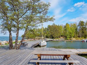 A wooden dock with a picnic table, a sailboat docked at a marina, and a calm lake with trees in the background.