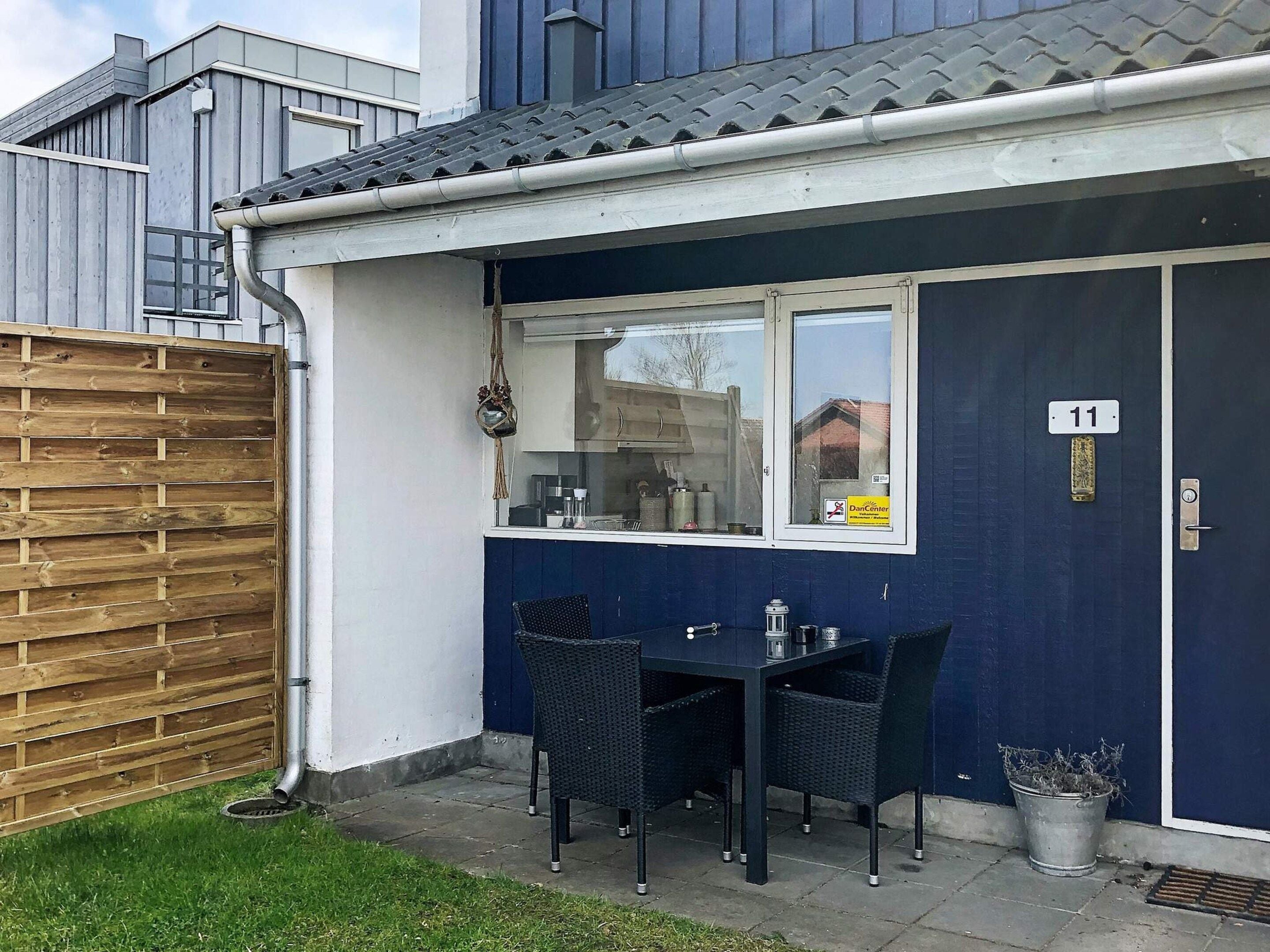 A small outdoor seating area with a table and chairs, a window, and a door with the number 11.
