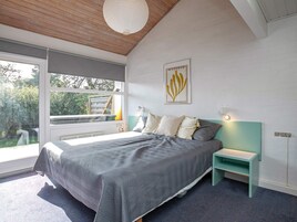 Et moderne soveværelse med en stor seng, et natbord, en lampe på væggen og et vindue med udsigt til grøn natur.