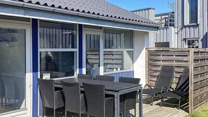 An outdoor patio with a table and chairs, a wooden deck, and a view of a building with large windows. - Holiday Home in VÃ¦ggerlÃ¸se (Vaeggerlose)