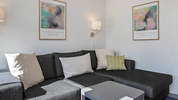 A modern living room with a grey sectional sofa, a small white table, and two abstract paintings on the walls.