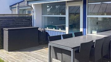 Een terras buiten met een tafel en stoelen, een overdekte zithoek en uitzicht door een glazen deur.