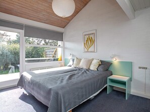 Ein modernes Schlafzimmer mit einem großen Bett, einem Fenster mit Blick auf Grünflächen, einem Wandbild und einem Nachttisch mit einer Lampe.