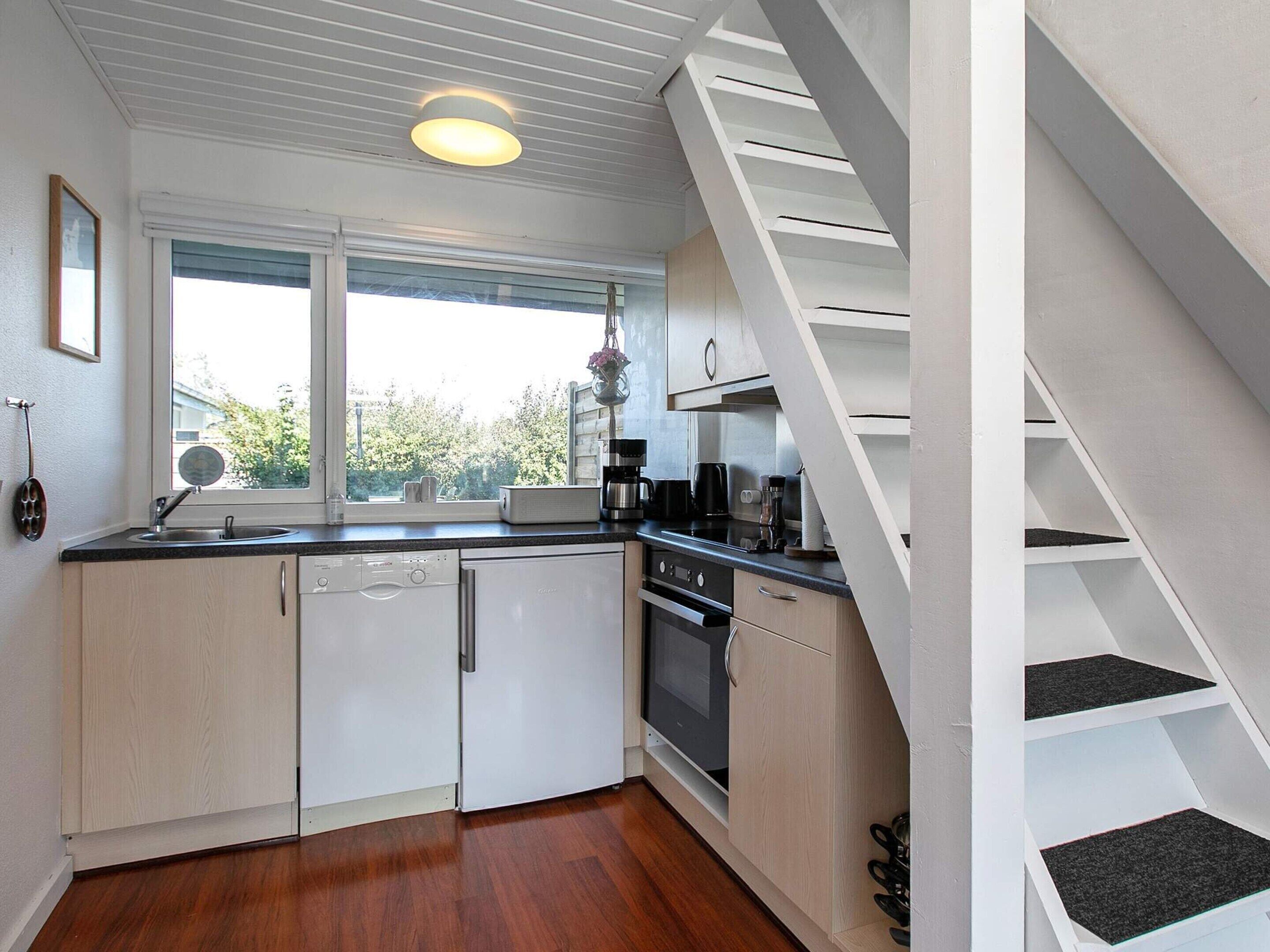 A compact kitchen with a dishwasher, stove, and a window with a view of greenery.