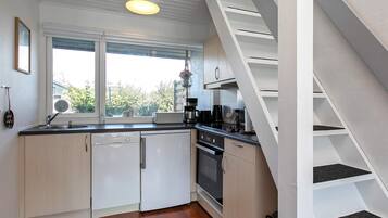 A compact kitchen with a dishwasher, stove, and a window with a view of greenery.