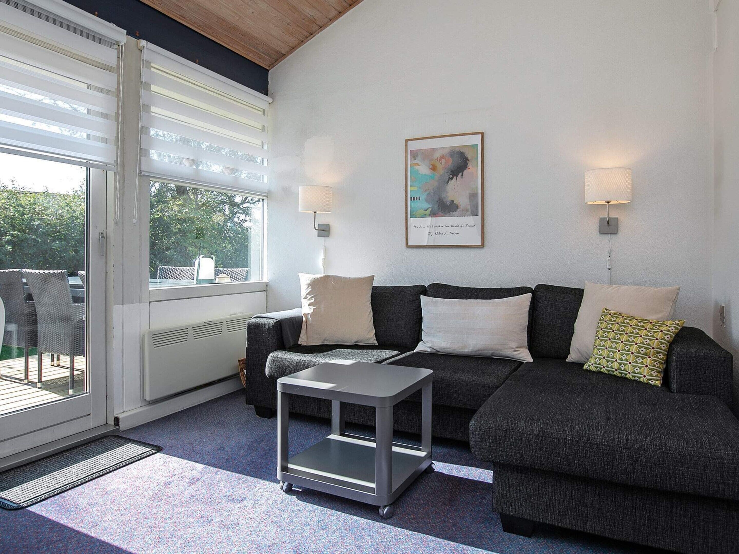 A modern living room with a grey sofa, a small side table, and a window with blinds.
