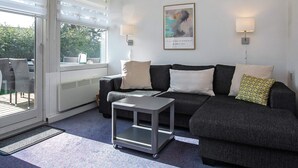 A modern living room with a grey sofa, a small side table, and a window with blinds. - Holiday Home in VÃ¦ggerlÃ¸se (Vaeggerlose)
