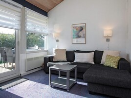 En moderne stue med en grå sofa, et lille sofabord og et vindue med persienner.