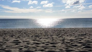 A beach with a clear sky and the sun reflecting on the water.
