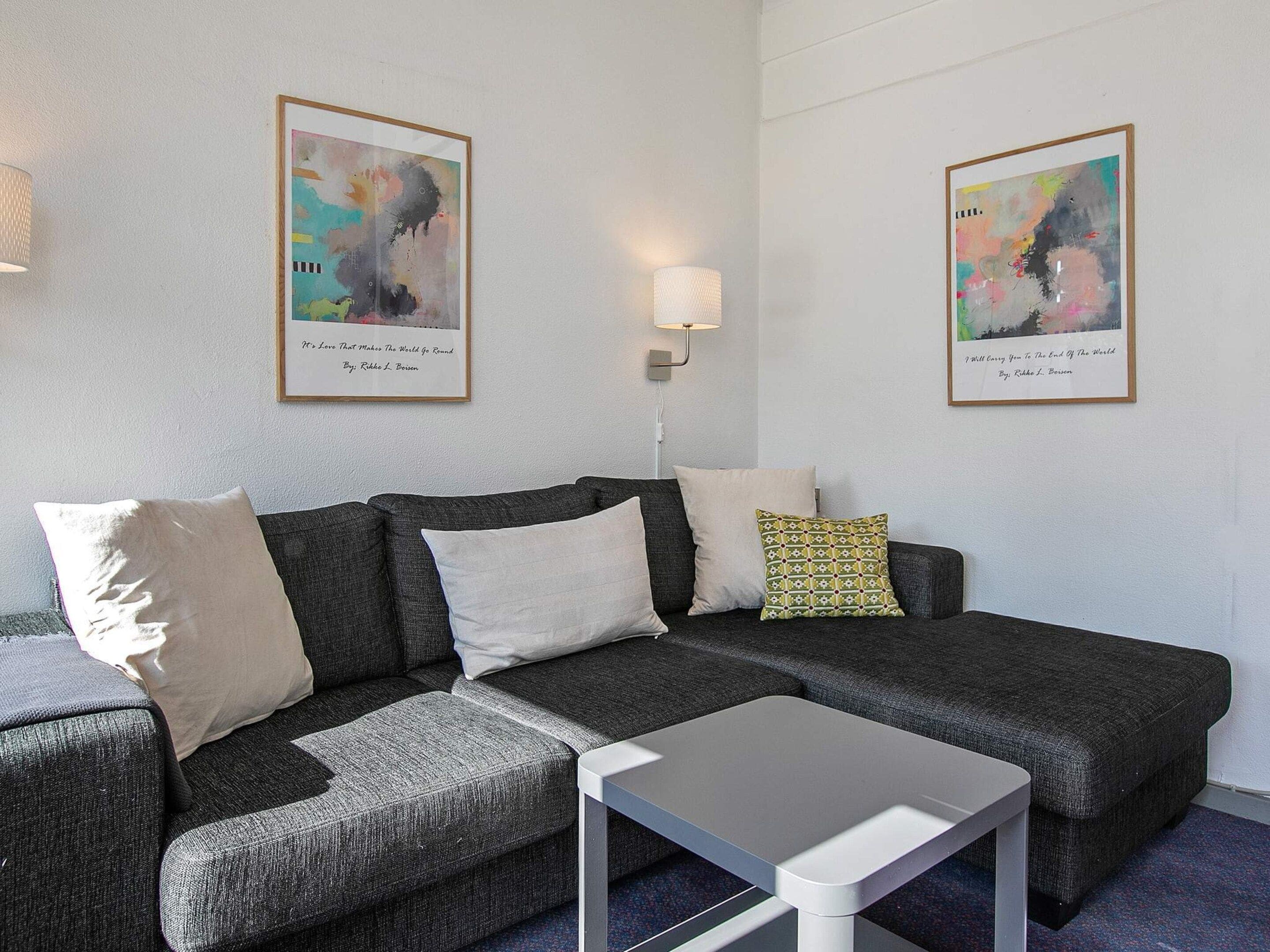 A modern living room with a grey sectional sofa, a white coffee table, and two framed abstract paintings on the wall.