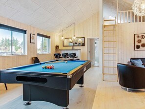 A pool table with balls, a pool table, and a chair in a room with wooden walls and a window. - Holiday Home in Blåvand (Blavand)
