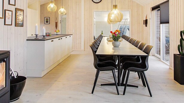 A modern kitchen with a central island, pendant lights, and a dining area with a long table and chairs. - Holiday Home in Blåvand (Blavand)