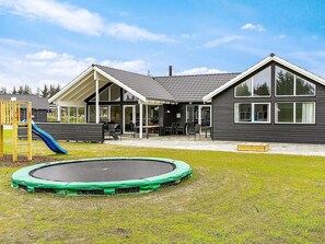 A modern house with a covered patio, a trampoline, and a children's play area. - Holiday Home in Blåvand (Blavand)