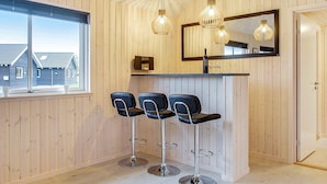 A modern bar area with wooden paneling, three black bar stools, and pendant lighting. - Holiday Home in Blåvand (Blavand)