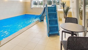 An indoor swimming pool with a blue slide, tiled floor, and seating area with tables and chairs. - Holiday Home in Blåvand (Blavand)