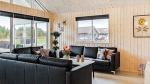A modern living room with black leather sofas, a wooden floor, large windows, and a ceiling light fixture. - Holiday Home in Blåvand (Blavand)