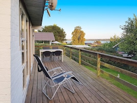 A wooden deck with a table and chairs, overlooking a body of water and greenery.