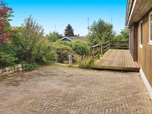 A wooden deck leading to a house with a brick pathway.
