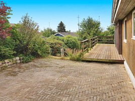 Una terraza de madera que conduce a una casa con un camino de ladrillo.