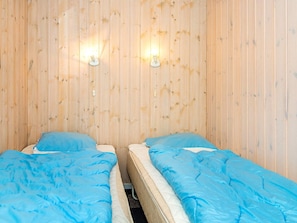 A room with two beds, each with a blue bedspread, against a wooden wall with two wall-mounted lights. - Holiday Home in BÃ¸rkop (Borkop)