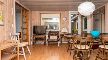 Un interior de madera con una televisión, una mesa de comedor, sillas y un reloj en la pared.