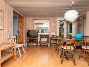 Un interior de madera con una televisión, una mesa de comedor, sillas y un reloj en la pared.