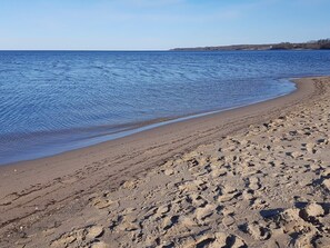 Une plage parsemée d’empreintes, un ciel dégagé et une côte lointaine.