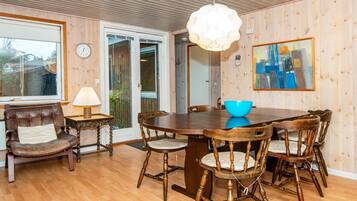 Un comedor con una mesa y sillas de madera, un cuenco azul, una lámpara y un cuadro en la pared.
