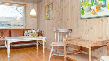 Una habitación con suelo de madera, una mesa blanca con velas, un sofá marrón, una silla de madera y un cuadro en la pared.