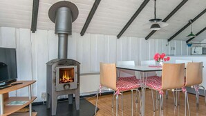 Une pièce chaleureuse avec un poêle à bois, une table à manger avec des chaises et un téléviseur posé sur un meuble.