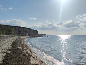 A beach with a sandy shore, a cliff, and a calm sea under a clear sky.