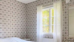 A bedroom with a bed, a window with curtains, a chair, and patterned wallpaper. - 4 Person Holiday Home in Skanes-fagerhult (Skånes Fagerhult)