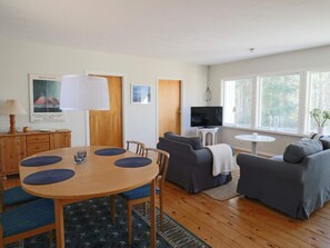 A living room with a round wooden table, two sofas, a TV on a small table, and a window with a view of trees.