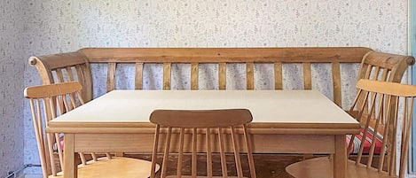 Een houten bank met een witte kussens, twee houten stoelen en een rode hanglamp.