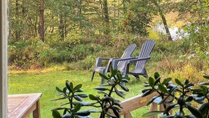 A deck with two Adirondack chairs facing a grassy area with trees and a body of water. - 4 Person Holiday Home in Skanes-fagerhult (Skånes Fagerhult)