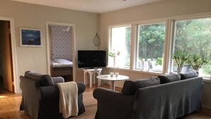 A cozy living room with a sofa, a TV, a small table, and a window with a view of greenery. - 4 Person Holiday Home in Skanes-fagerhult (Skånes Fagerhult)