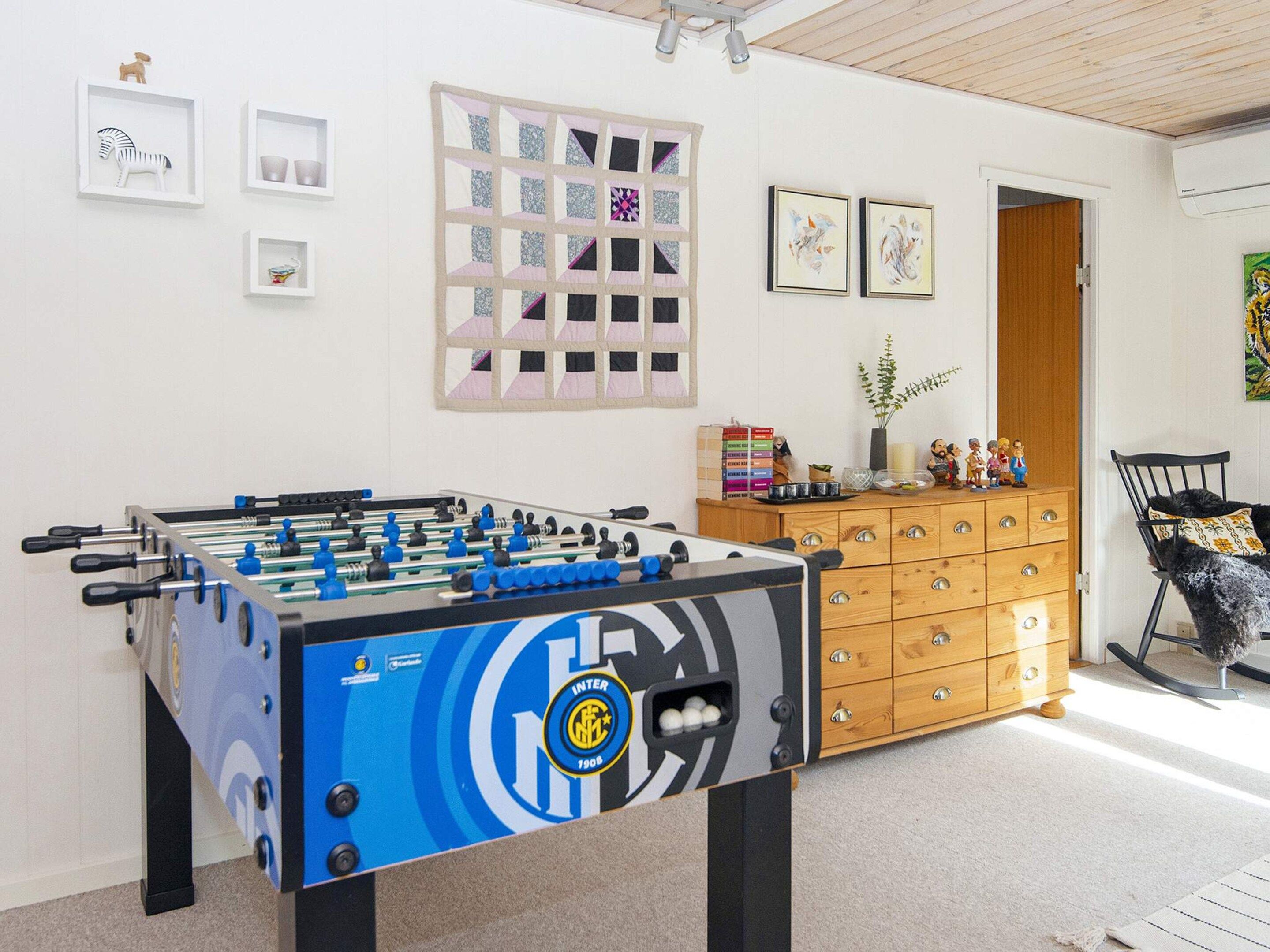 Una habitación con mesa de fútbol, cómoda de madera y una silla.