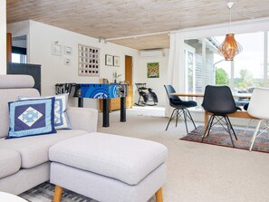 A modern living room with a sofa, ottoman, and a foosball table. There is a dining area with chairs and a table. - Holiday Home in Ebeltoft (Ebeltoft)