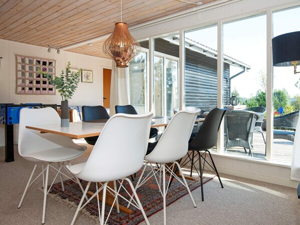 A modern dining area with a wooden table and chairs, large windows, and a view of the outdoors. - Holiday Home in Ebeltoft (Ebeltoft)